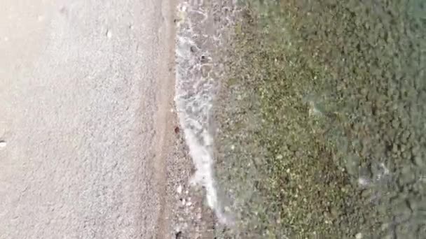 Vista dall'alto di ciottoli sotto l'acqua limpida e le onde calme del mare rotolando sulla sabbia bianca della spiaggia. Armonia e tranquillità concetto — Video Stock