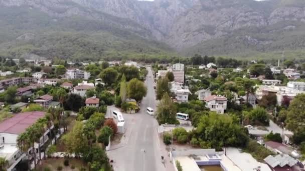 Vue aérienne d'une ville de montagne avec de belles maisons et chalets au milieu de la verdure et un groupe d'autobus sur la route centrale — Video