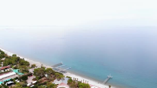 Дронна зйомка пляжної зони відпочинку з рядами шезлонгів і пірсів і видом на блакитне спокійне море в білому тумані — стокове відео