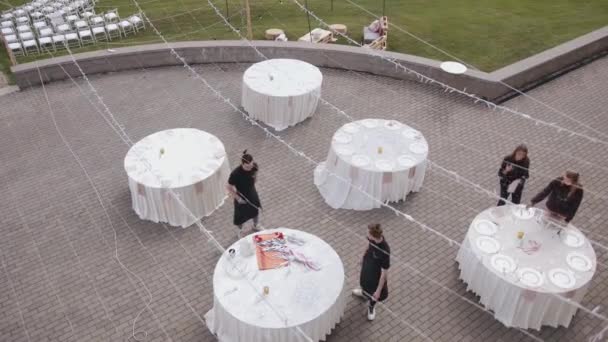 Belarus. MinskAugust 21, 2021: Aerial view of waiters in black uniform arranging dishes and cutlery on tables for a wedding celebration on the terrace of a country estate — стоковое видео