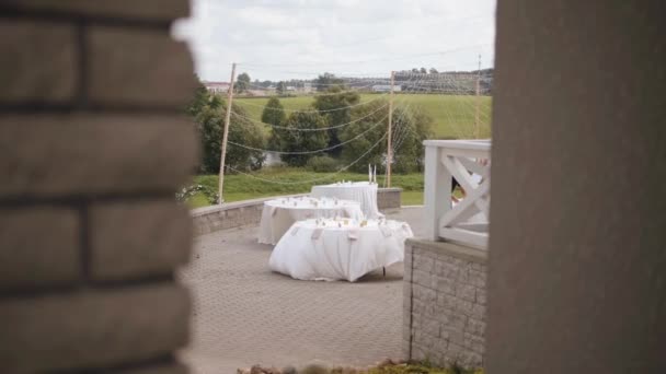 Вид на терасу, прикрашену для весільної церемонії, подають столи з білими скатертинами, підірваними вітром. Підглянутий — стокове відео