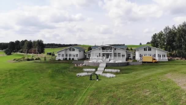 Flygfoto över en stuga på landet med terrass med bord och gräsmatta med blomsterbåge och stolsrader för gäster vid en bröllopsceremoni — Stockvideo