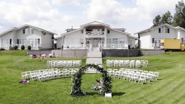 Drone shooting of the flower arch decoration and tables setting on the terrace of a complex of three cottages for a wedding ceremony — 图库视频影像