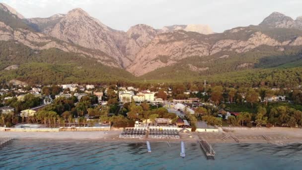 山間の海辺にある小さなリゾートタウンの空中ビューとプール付きのビーチやホテルのサンラウンジャーの行 — ストック動画