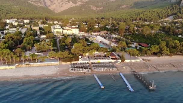 Вид з повітря на ряди шезлонгів на морському пляжі і великий готель з безліччю басейнів на березі гірського міста — стокове відео