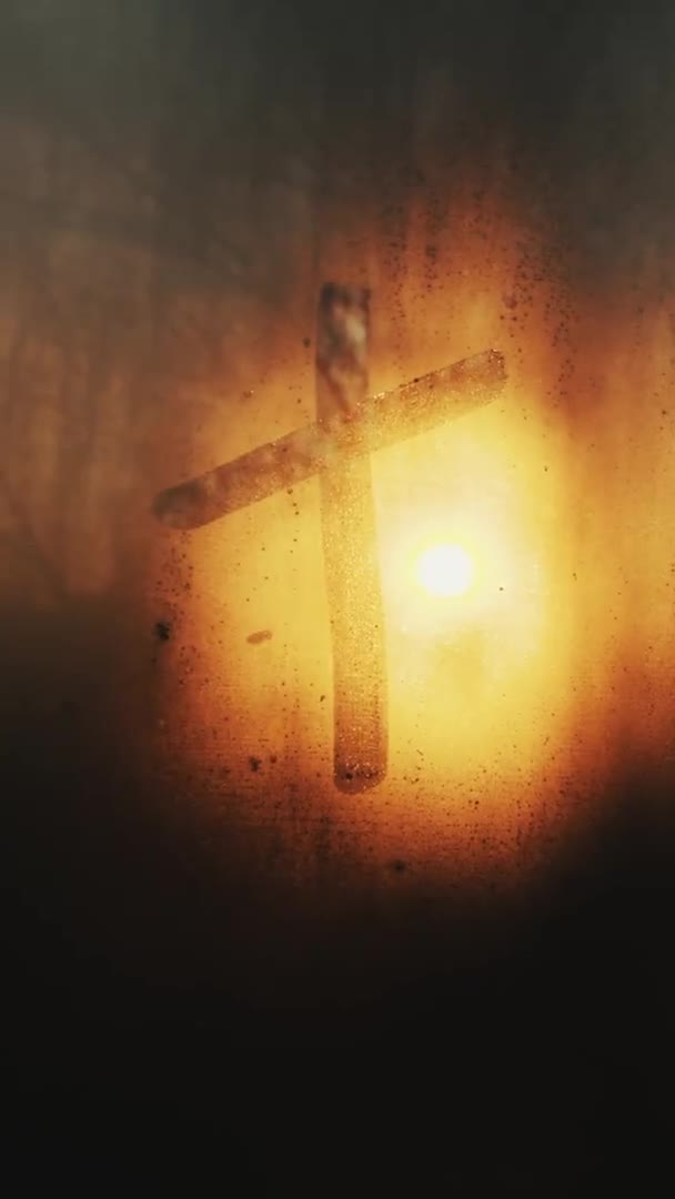 A keresztet egy ujjal húzzák egy ködös ablakon a narancssárga nap hátteréhez. Függőleges videó — Stock videók