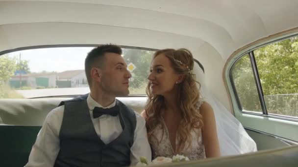 The newlyweds in love are driving in the back seat of a retro car and the tender bride sniffs the bouquet and sticks his hand out the window. Slow motion — Stockvideo