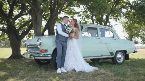 Λευκορωσία. Περιοχή Γκόμελ. 21 Αυγούστου 2021: Ο γαμπρός αγκαλιάζει τη νύφη με ένα μπουκέτο στο φόντο ενός λευκού ρετρό Volga Gaz 21 — Αρχείο Βίντεο