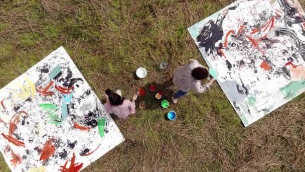 Aerial view of young girls who are painting abstract pictures on canvases lying on a wheat field. Art and realization concept — Stockvideo