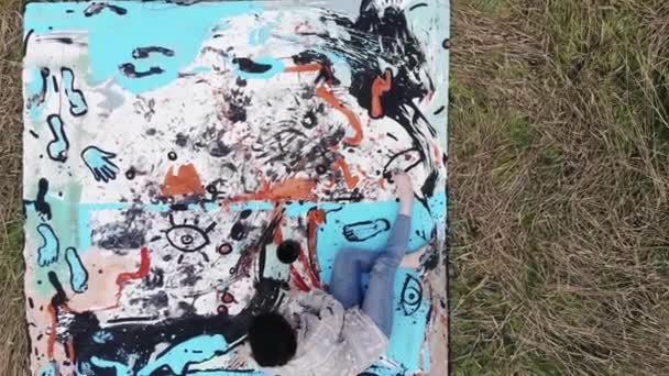 Aerial view of a young girl sitting on a canvas in a wheat field and painting a picture in an avant-garde style. Modern art concept — Vídeo de Stock