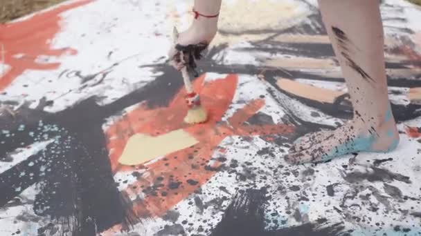 A talented young girl goes barefoot on a canvas in a wheat field and paints an abstract picture with a brush. Creativity concept — Vídeo de Stock