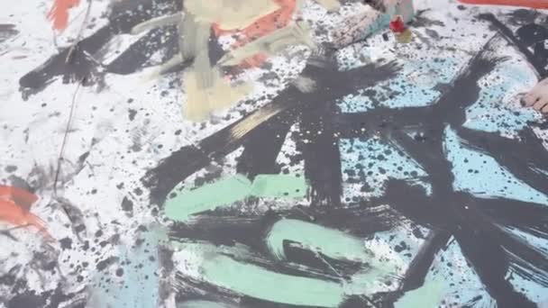 A talented young artist with bare feet stained with paint draws a creative abstract picture with a brush on a canvas in a wheat field — Vídeo de Stock