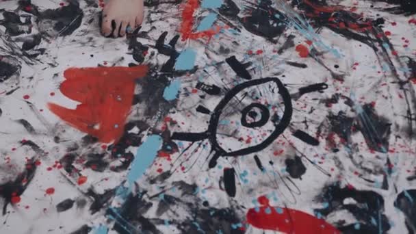Een jonge kunstenares met blote voeten gekleurd met verf gaat op een groot doek en schildert een creatief abstract beeld met een kwast — Stockvideo