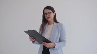 Konsantre genç iş kadını panoya iliştirilmiş belgeleri inceliyor ve beyaz izole edilmiş arka planda dururken gülümsüyor.