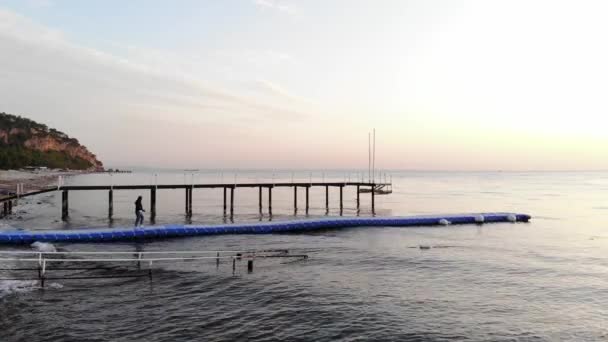 Aerial view of young girl going from the mountainous coast on plastic modular pier in calm sea. The concept of solitude and contemplation — Stockvideo