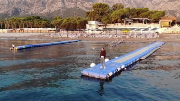 Shooting from drone of a young girl stands on a plastic modular pontoon among the waves of the sea. Contemplation and reflection concept — Video Stock