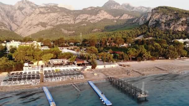 Вид з повітря на ряди шезлонгів на морському пляжі і великий готель з безліччю басейнів на березі гірського міста — стокове відео