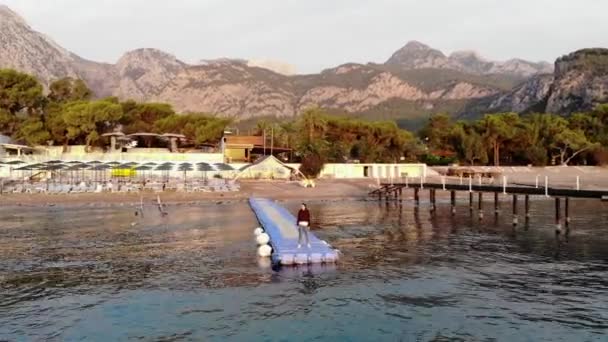 Tournage à partir d'un drone d'une jeune fille se tient sur un ponton modulaire en plastique parmi les vagues de la mer. Concept de contemplation et de réflexion. Concept de retraite. solitude dans la nature — Video