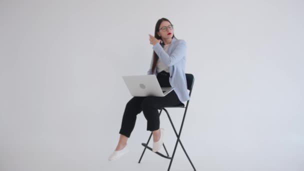 Ein schönes unabhängiges junges Mädchen mit Brille sitzt auf einem Hochstuhl und arbeitet an einem Laptop. Feminismus. Wahlfreiheit — Stockvideo