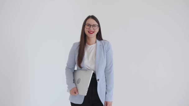 A beautiful young business woman is standing with a laptop under her arm and fooling around in front of the camera showing tongue — Vídeo de Stock
