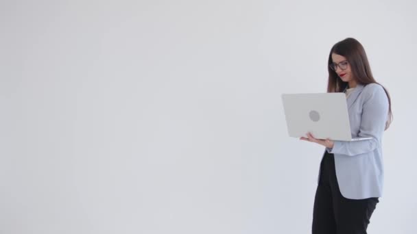 Concentrated young business lady is walking with a laptop back and forth on a white background and is typing on the keyboard — 图库视频影像