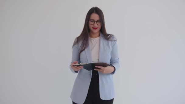 Zelfverzekerde jonge zakenvrouw staat tegen een geïsoleerde witte achtergrond en houdt een klembord in haar handen. Loopbaan- en succesconcept — Stockvideo