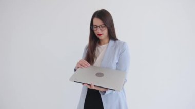 Ciddi genç bir iş kadını dizüstü bilgisayarını elinde tutuyor ve izole beyaz arka planda dururken gizli parmak izlerini açıyor.