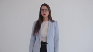 Güzel, genç bir iş kadını beyaz, izole bir arka planda duruyor ve kibirli bir bakışla kollarını göğsünde kavuşturuyor.