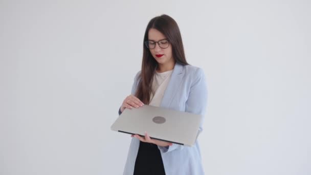 Serious young business woman holding a laptop in her hands and opening its cover prints while standing on isolated white background