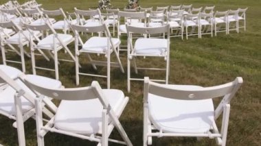 A place for a wedding ceremony on the lawn by the river with an arch decorated with white flowers and rows of chairs for guests