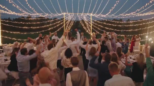 Belarus. MinskAugust 21, 2021: The bride and groom dance together with guests on an open terrace with laid tables and decorated with glowing garlands — Αρχείο Βίντεο