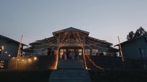 Belarus. MinskAugust 21, 2021: Little boys run down the stairs from the terrace of the cottage decorated with glowing garlands where the party is taking place. Slow motion — стокове відео