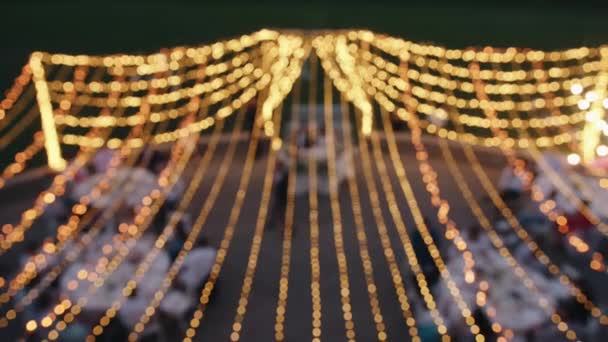 Aerial view of rows of glowing garlands on the terrace during the party with the newlyweds and guests at the tables. Bokeh effect — Video Stock
