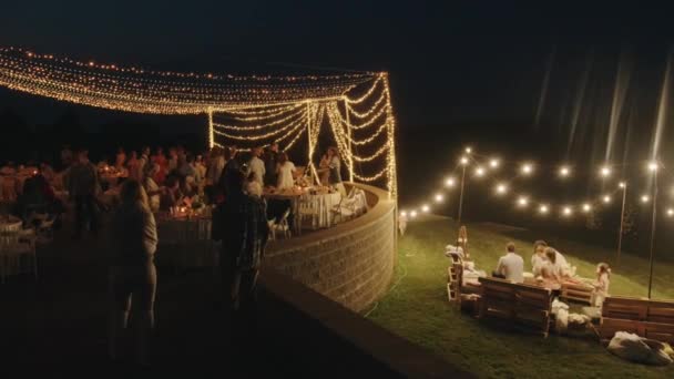 Beyaz Rusya. Minsk21 Ağustos 2021: Yeni evliler ve konuklar düğün kutlamaları sırasında parlayan çelenklerle süslenmiş bir verandada oturup dans ediyorlar — Stok video