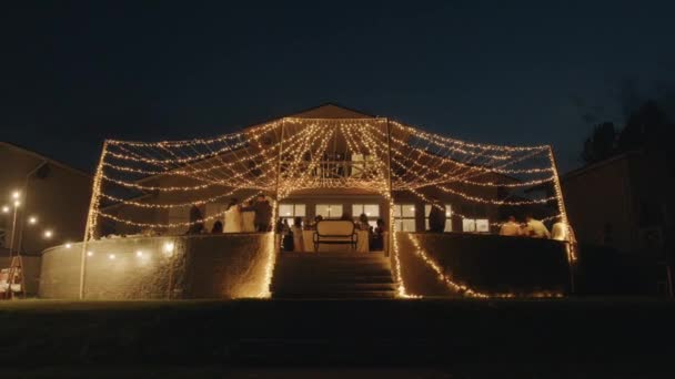 View of the terrace of a cottage decorated with rows of garlands during a wedding celebration on a summer evening. Slow motion — Video