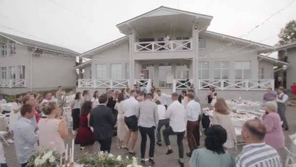 Bielorrusia. MinskAgosto 21, 2021: Los huéspedes bailan y se burlan de realizar las tareas del anfitrión de la boda en la terraza de una hermosa casa de campo — Vídeos de Stock