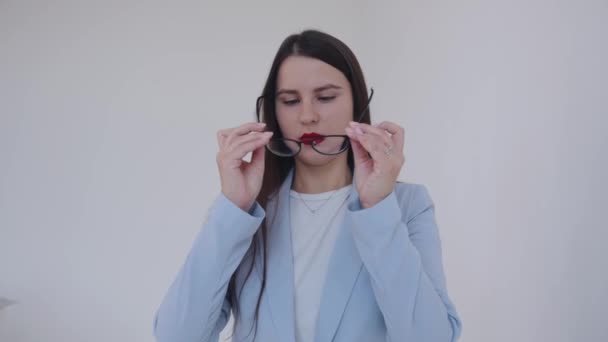 Die seriöse junge Geschäftsfrau nimmt die Brille ab und glättet ihre Haare vor einsamem weißen Hintergrund. Karriere- und Erfolgskonzept — Stockvideo