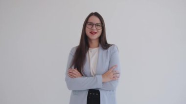 Olağanüstü genç iş kadını kollarını göğsüne bağlamış beyaz izole bir arka planda duruyor ve bulaşıcı bir şekilde gülüyor.