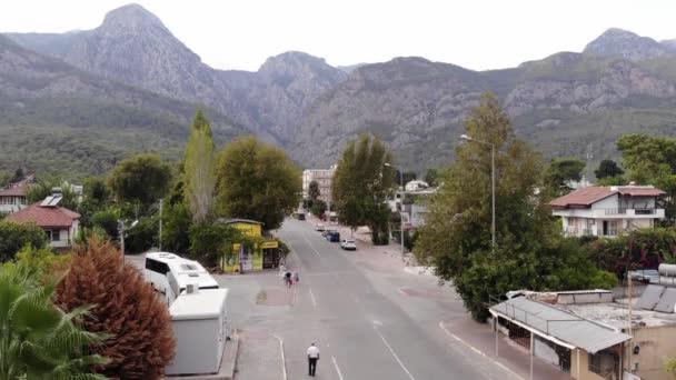 Türkei, Kemer - 20. Oktober 2021: Luftaufnahme einer wunderschönen Stadt zwischen Bäumen am Fuße der Berge und regem Verkehr auf der zentralen Straße — Stockvideo