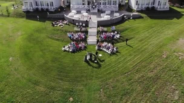 Top view of a country cottage terrace with tables and rows of chairs with guests on the lawn during a wedding ceremony — Stock Video
