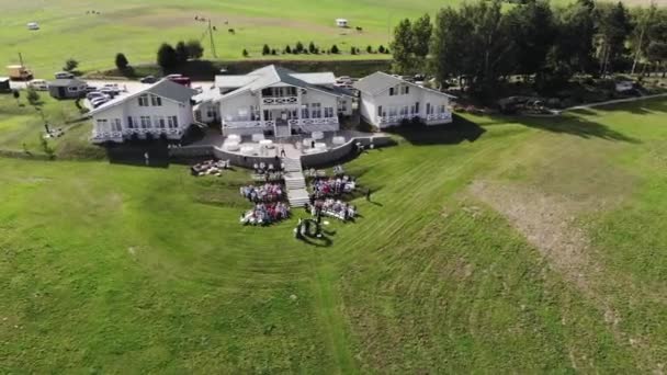 Top view of a country cottage terrace with tables and rows of chairs with guests on the lawn during a wedding ceremony — Stock Video