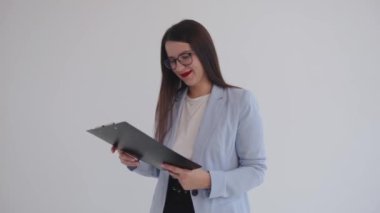 Konsantre genç iş kadını panoya iliştirilmiş belgeleri inceliyor ve beyaz izole edilmiş arka planda dururken gülümsüyor.