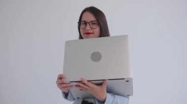 Siyah gözlüklü, kendine güvenen genç bir iş kadını dizüstü bilgisayarın arkasından bakıp hayal kuruyor.