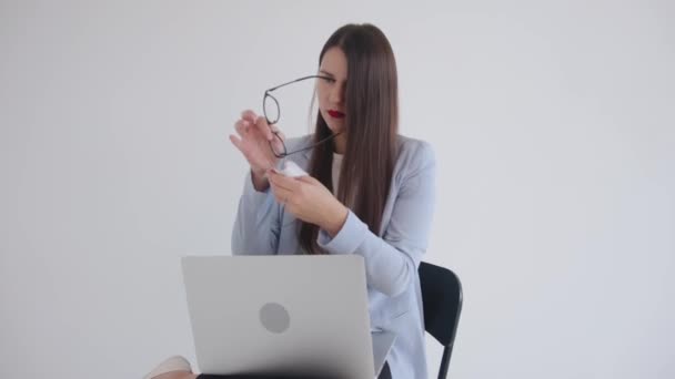 Una hermosa mujer de negocios joven se sienta en una silla con una computadora portátil en su regazo y se limpia las gafas con una servilleta. Concepto de éxito y carrera — Vídeo de stock