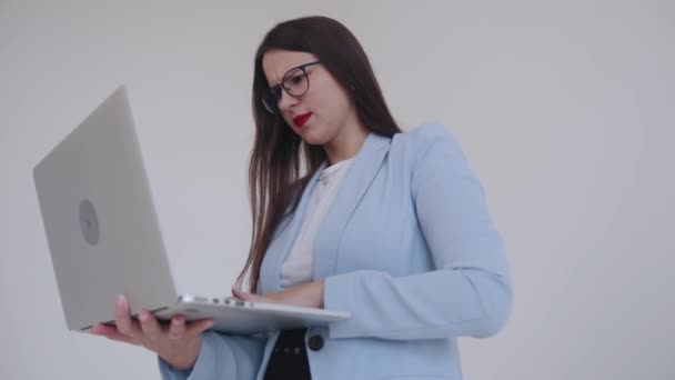 O tânără femeie de afaceri spectaculoasă care lucrează pe un laptop în timp ce stă pe un fundal alb. Feminism. Carieră. Femeie putere — Videoclip de stoc