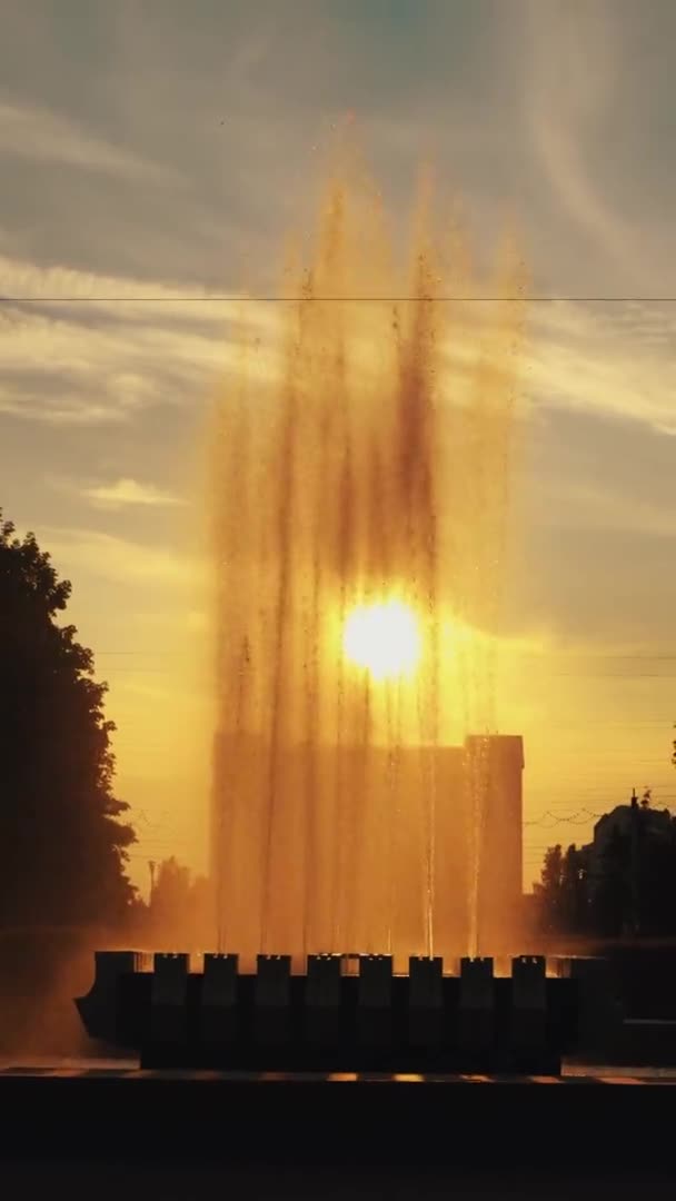 De höga jetstrålar av fontänen mot bakgrund av solnedgången och flicka som löper längs parapet. Vertikal video. Långsamma rörelser — Stockvideo