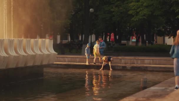 Minsk, Bielorrusia - 29 de junio de 2021: Los niños juegan en la fuente de la ciudad y las palomas vuelan alrededor de la cascada de agua al atardecer. Descanso familiar. Movimiento lento — Vídeo de stock