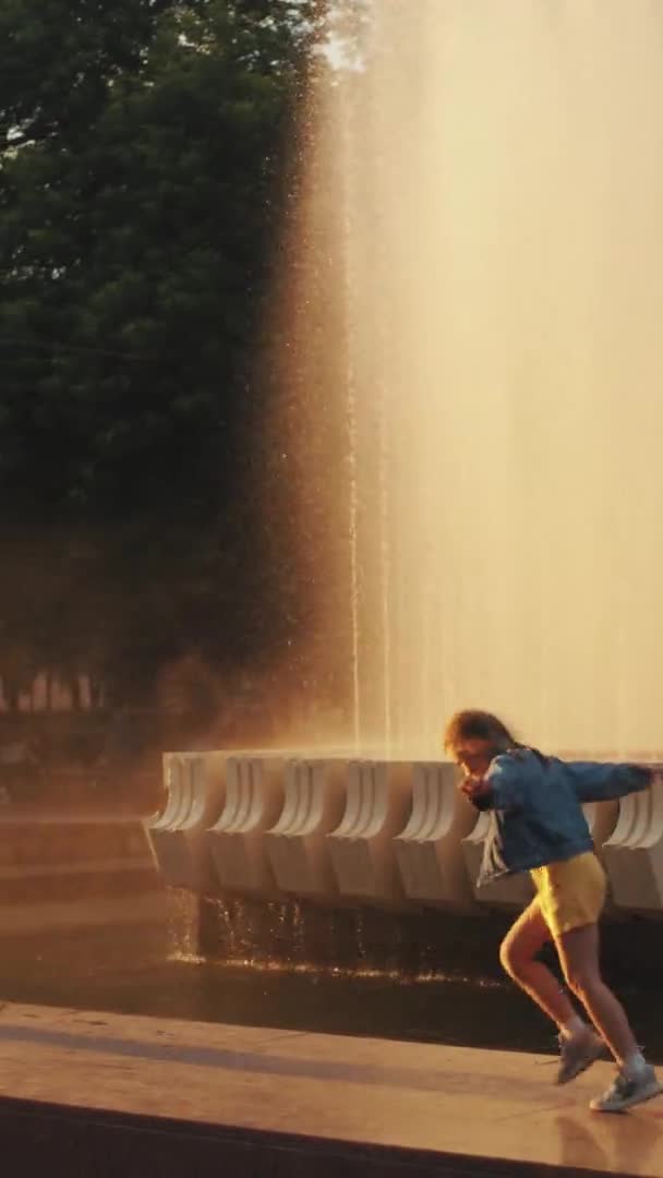 Minsk, Bielorrússia - 29 de junho de 2021: Crianças felizes brincam perto da fonte e correm com os braços estendidos sob os salpicos de água. Movimento lento. Vídeo vertical — Vídeo de Stock