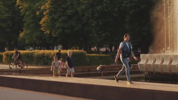 Minsk, Bielorrusia - 29 de junio de 2021: Las familias se relajan en el parque de la ciudad en una noche de verano y los niños de diferentes edades caminan a lo largo del parapeto alrededor de la fuente. Movimiento lento — Vídeo de stock
