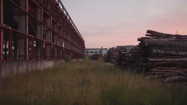 Kereste kamyonu ve çimenlerin üzerindeki kereste yığını gün batımında metal yapıları olan açık bir fabrika deposunun yanında.